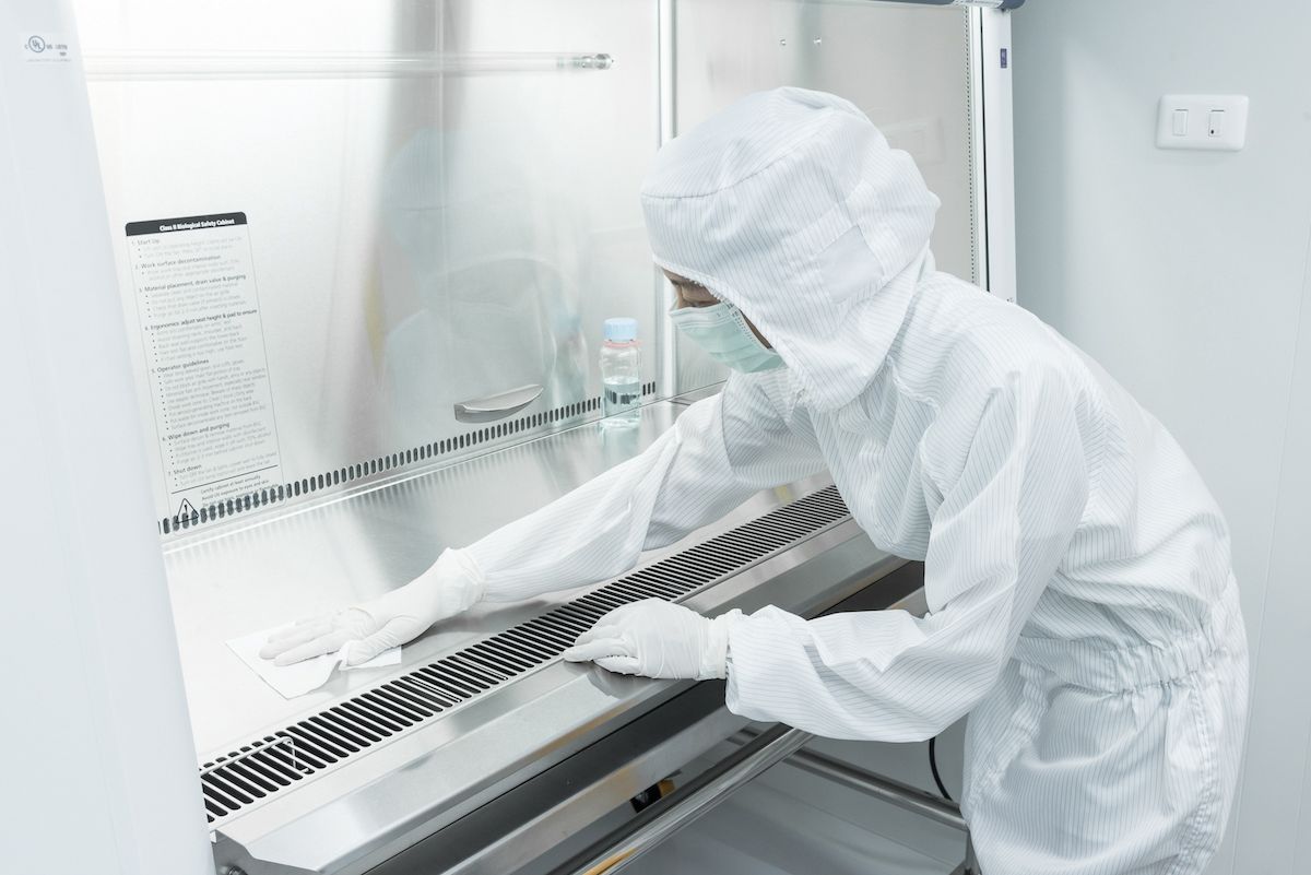 A scientist in sterile coverall gown using alcohol 70% and cleanroom wipes for cleaning Biological safety cabinet(BSC.) in laboratory, before and after using bsc. ,decontamination,Cleanroom facility.